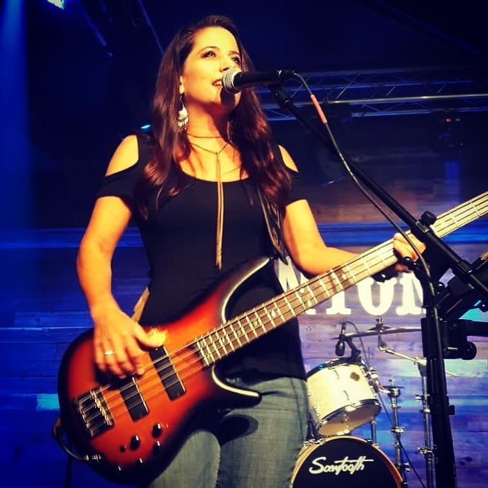 image of Kim Martin playing live music on stage playing the bass and singing into a microphone